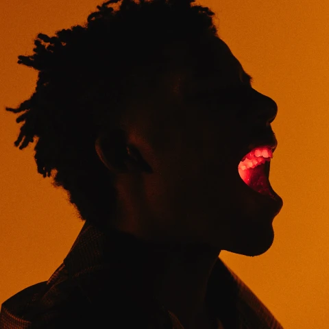 Person in silhouette yelling with glowing light in their mouth, set against an orange background.
