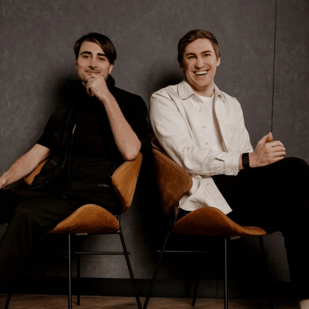 Two people seated, smiling; one in a white shirt, the other in a dark vest.