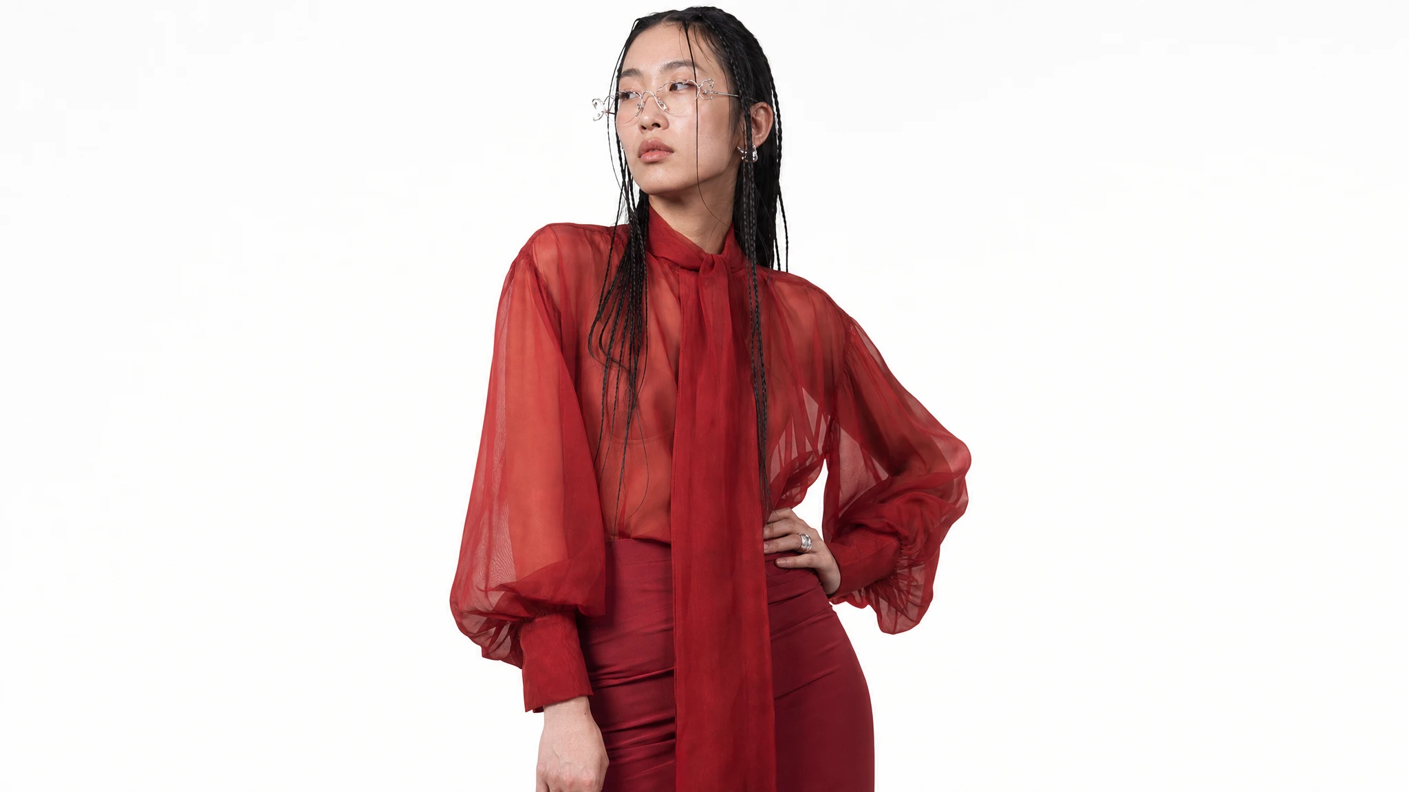 Person wearing a sheer red blouse and glasses against a white background.